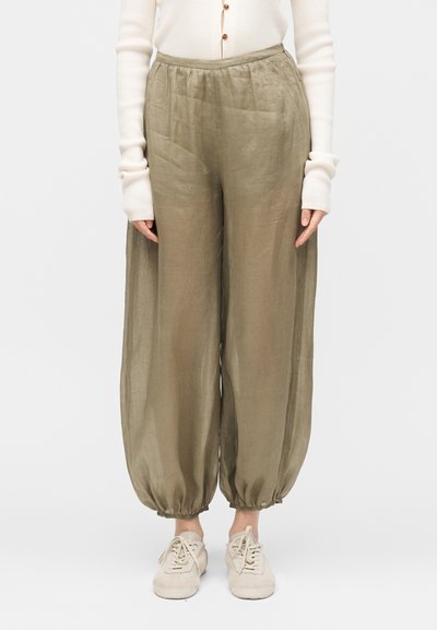 Femme portant un pantalon large vert olive avec les chevilles resserrées, un haut blanc à manches longues et des chaussures beiges à lacets.