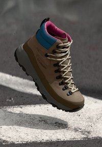 Bottes de randonnée marron avec des accents turquoise et rose, dotées d'un dessus texturé, de lacets ronds et d'une semelle robuste pour une meilleure adhérence.