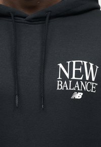 Μαύρο φούτερ με κουκούλα με λευκό κείμενο "NEW BALANCE" και λογότυπο στο στήθος, με πλεκτά κορδόνια με μεταλλικές άκρες.