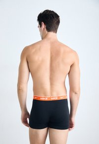 Fekete boxernadrág narancssárga Nike derékkal. Az anyag simának tűnik; a dizájn testhez simuló, középmagas szabású.