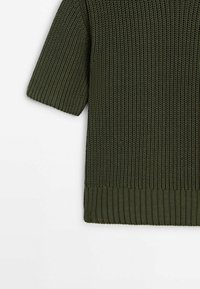 Kortærmet, tekstureret top i mørkegrøn, med et ribstrikket design og en kraftig ribbet kant forneden for ekstra struktur.