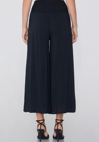 Culottes noires à jambe large en tissu léger avec une taille smockée, présentant une texture lisse et un design fluide.