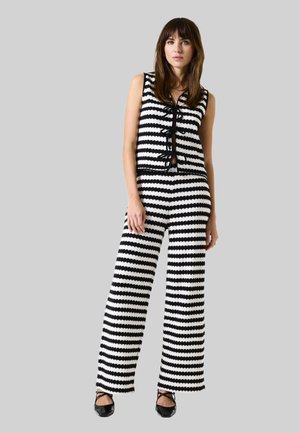 Black and white striped knit jumpsuit with a sleeveless design, featuring a placket with bows and wide-leg pants. Accented with black trim.