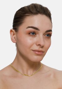 Collier doré avec deux fils entrelacés. Design lisse et léger qui reflète la lumière, ajoutant un éclat subtil. Convient pour le superposition.