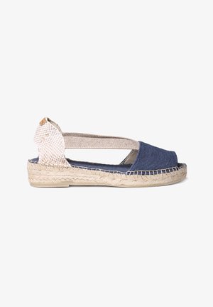 Tengerészkék vászon espadrille, fonott bézs hátsó résszel, nyitott toe dizájnnal és fonott juta talppal. Rugalmas heveder a biztonságos illeszkedés érdekében.