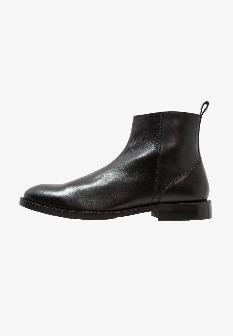 Bottine en cuir noir avec petit talon, bout arrondi, couture latérale et languette à l'arrière.