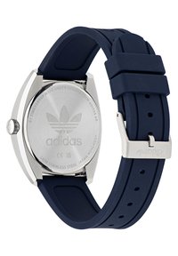 Montre avec bracelet en silicone bleu marine et boîtier en acier inoxydable, affichant un fond argenté gravé du logo Adidas et des détails de résistance à l'eau.
