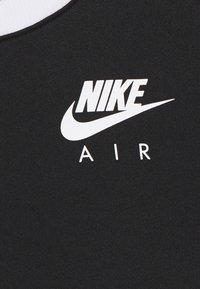 Bílé logo "NIKE AIR" se symbolem swoosh na černém texturovaném pozadí.