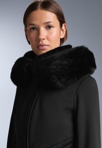 Czarna, ocieplana kurtka z dużym futrzanym kołnierzem. Posiada ukośne przeszycia na tkaninie oraz wysoki kołnierz dla dodatkowego ciepła.