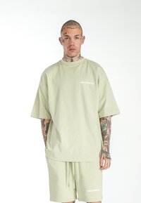 Camiseta oversized de color verde claro y pantalones cortos a juego en tela suave. Presenta el logo "MULTIPLY" en blanco, mangas cortas y un corte relajado.
