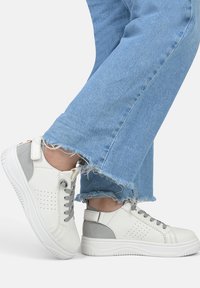 Weiße und graue Sneakers mit perforierten Details, Schnürdesign und Gummisohle; kombiniert mit ausgefranstem blauen Jeans.