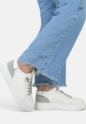 Witte en grijze sneakers met geperforeerde details, vetersluiting en rubberen zool; gecombineerd met versleten blauwe denim jeans.