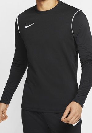Homme portant un haut de sport noir à manches longues Nike avec logo swoosh blanc et passepoil blanc aux épaules sur fond uni.