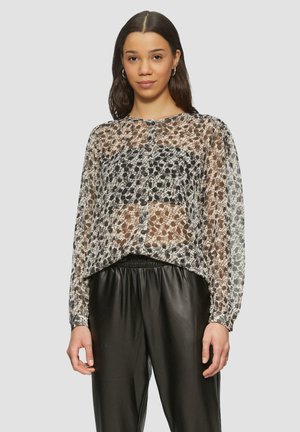 Doorzichtige blouse met lange mouwen en een bloemenpatroon in zwart, bruin en crème. Heeft een afgeronde zoom en sluiting met knopen aan de voorkant. Gecombineerd met zwarte broeken.