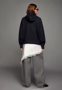 Mörkblå stickad hoodie med avslappnad passform, lager-på-lager över en vit satinklänning med spetskant, kombinerad med vida grå byxor.