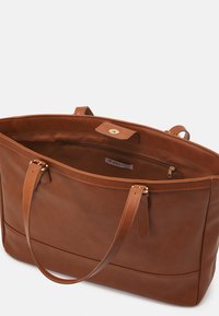 Brun læder tote taske med glat tekstur, åben top, to håndtag, guldfarvet hardware og en indvendig lynlåslomme. Logoet er synligt indeni.