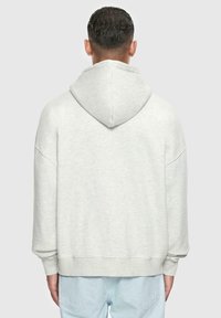 Lys grå oversized hoodie med snoretræk i huen, blød tekstur, sænkede skuldre og ribbede ærmer. Simpelt design uden synlige mønstre.