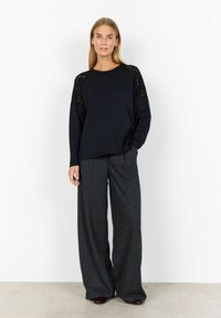 Black long-sleeve top with lace accents at shoulders, paired with wide-leg gray textured trousers. Smooth fabric with relaxed fit.