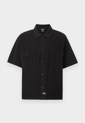Camicia nera a maniche corte con bottoni, due tasche frontali con patta e una piccola etichetta con il marchio al centro in basso.