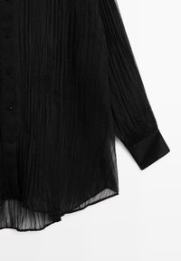 Blusa nera plissettata con maniche lunghe, bottoni sulla parte anteriore, orlo curvo e polsini morbidi, realizzata in tessuto traslucido leggero.