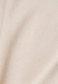 Lys beige ribbet stof, der viser en fin struktur med subtile lodrette linjer, blød overflade og strækbar kvalitet.