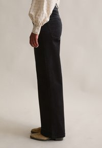 Zwarte corduroy broek met wijde pijpen en verticale ribbels, voorzien van een hoge taille en zijzakken, gedragen met tankleurige schoenen met blokhakken.