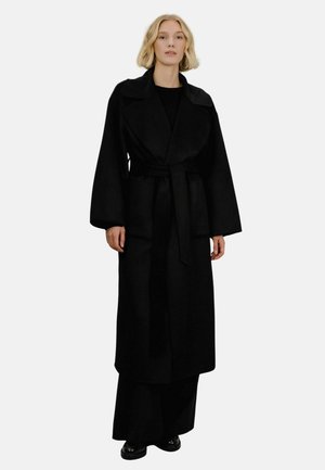 Svart ull trenchcoat med brede revers, lange ermer og belte. Har en avslappet passform og sidelommer. Glatt tekstur.