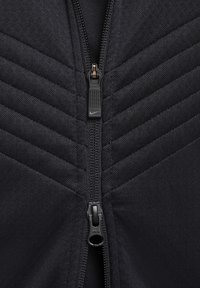 Zwarte zip-up jack met een gewatteerde diagonale textuur, voorzien van een stevige YKK-rits en Nike-branding op de rits. 