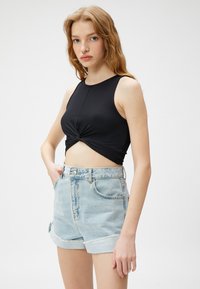 Top corto negro de canalé con un nudo en el frente, combinado con pantalones cortos de mezclilla azul claro con dobladillos enrollados y un diseño de cintura alta.