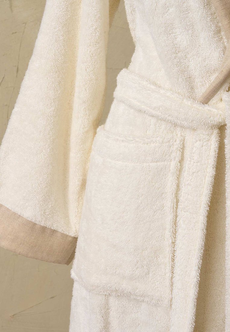 Crème-kleurige badjas van badstof heeft een zachte textuur, brede mouwen, een bijpassende riem en een contrasterende beige rand op de manchetten en zakken.