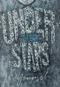 Grå t-shirt med stor, djärv vit text i intrikata mönster och mindre turkosa accenter. Mjuk, texturerad tyg med rund halsringning.