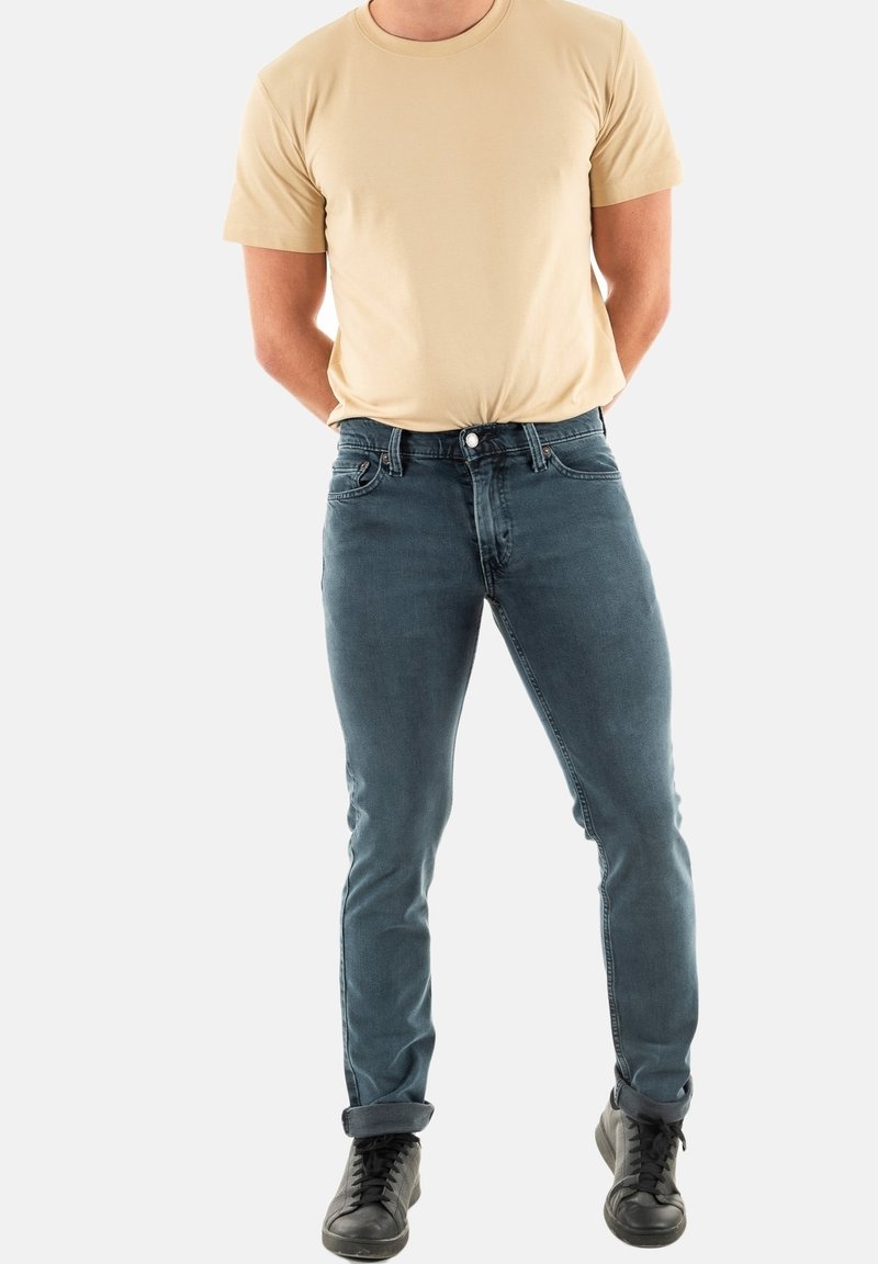 Jeans ajustados de mezclilla azul oscuro con una textura suave, combinados con una camiseta de manga corta beige y zapatillas negras. Diseño simple, sin patrones visibles.