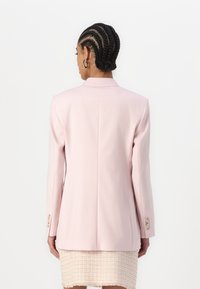 Bledě růžový blazer se strukturovanou siluetou, s jedním zadním rozparkem, dlouhými rukávy a dekorativními knoflíky na manžetách.