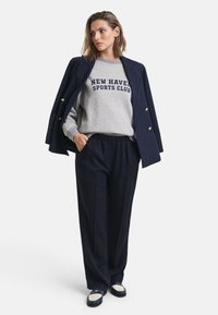 Felpa grigia con la scritta "NEW HAVEN SPORTS CLUB", blazer blu a righe verticali, pantaloni blu morbidi e mocassini blu con dettagli bianchi.