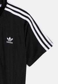 Juodas sportinis marškinėliai su trumomis rankovėmis, su trimis baltomis juostelėmis ant pečių ir baltu Adidas logotipu ant krūtinės.