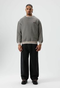 Gestreepte sweatshirt in beige en zwart, met een ronde hals en geribbelde boorden. Gevoerd met donkerzwarte wijde jeans en zwarte schoenen.