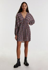 Schwarz gemustertes Kleid mit floralem Muster, langen Puffärmeln, tiefem V-Ausschnitt und gerafftem Bund. Tragen mit schwarzen Schuhen mit dickem Fußbett.