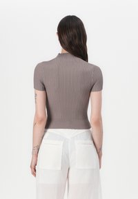 Korta ärmar, ribbad topp i taupe, med hög halsringning och en figurnära siluett. Bärs med vita, vida byxor med fickor.