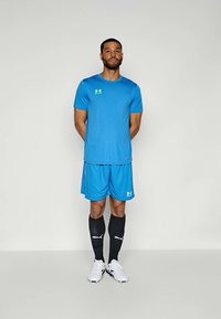 Ανοιχτό μπλε αθλητικό μπλουζάκι με αντίστοιχα σορτς, μαύρες κάλτσες και λευκά υποδήματα. Περιέχει λογότυπο στο μπλουζάκι και στα σορτς.