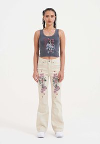 Top tank gris court avec un graphique de crâne, associé à un jean beige évasé avec une broderie florale et en forme de cœur éclatante sur les deux jambes.