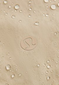 Gouttes d'eau sur un tissu beige avec un logo circulaire visible au centre, mettant en valeur la texture du matériau résistant à l'eau.
