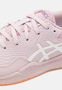 Světlé růžové sportovní boty s texturovaným syntetickým svrškem, bílými akcenty loga a flexibilní, polstrovanou podrážkou s jemným oranžovým nádechem.