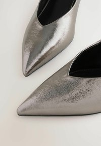 Chaussures pointues argentées métalliques avec une surface texturée, dotées d'une découpe basse autour du pied pour un design épuré et d'une doublure intérieure noire.