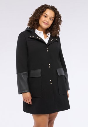 Cappotto nero con cappuccio, caratterizzato da dettagli in pelle sulle maniche, due tasche frontali e bottoni a scatto dorati sul davanti. Texture liscia.