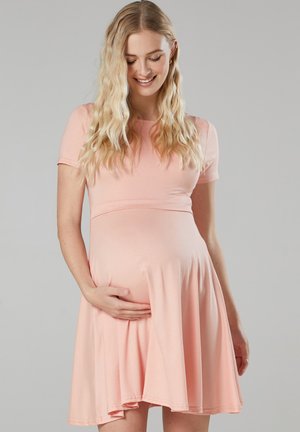 Light pink maternity dress with short sleeves, fitted bodice, and flared skirt, made of soft fabric, showing the wearer cradling a baby bump.