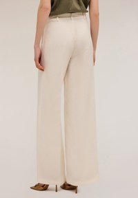 Wijde broek in lichtcrème stof met een gladde textuur, featuring een hoge taille en een op maat gemaakte uitstraling. Gepaard met bronzen hakken.