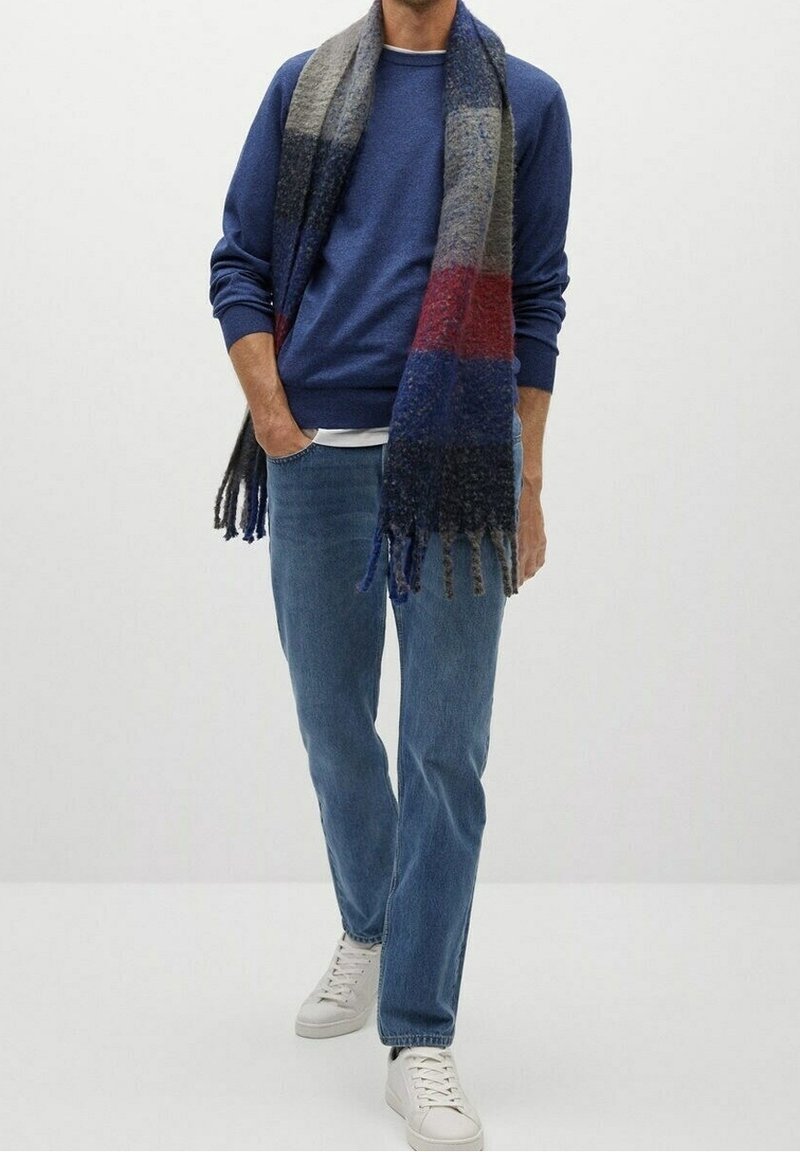 Suéter de punto azul, camiseta blanca, jeans de mezclilla claros y zapatillas blancas. Envueltos en una bufanda de rayas multicolores con flecos.