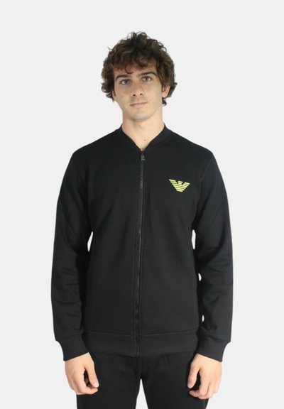 Felpa nera con zip, con collo tondo, polsini e vita a costine. Presenta un piccolo logo giallo sul petto. Tessuto dalla texture liscia.