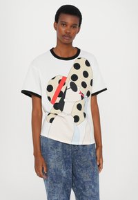White T-shirt with a graphic design featuring a woman in a large polka-dotted hat, surrounded by a black and red accent. Short sleeves.