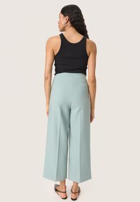 Črn rebrast tank top v kombinaciji z svetlo zelenimi širokimi hlačami. Hlače imajo čist dizajn z gladko teksturo in elegantno silhueto.